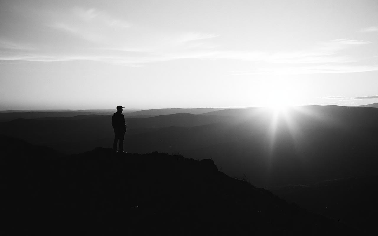 A figure standing on a ridge at sunrise looking over hills.